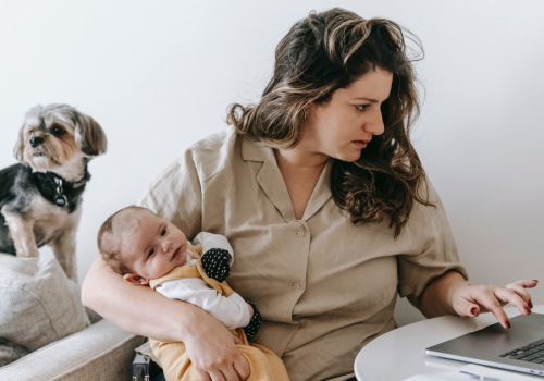 Working mother holding baby types on laptop with dog nearby