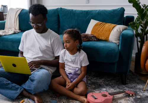 Dad and daughter looking at laptop screen while sitting on the floor in front of a couch
